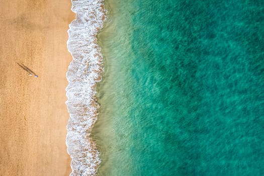 Aerial view of the walking people on the white sandy beach near sea with waves at sunset. Summer holiday. Top view of sporty people, clear azure water. Lifestyle and sport