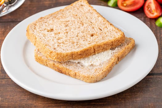 Cream cheese sandwich on white porcelain plate on wooden table