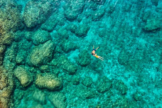 Aerial view of a young couple snorkeling above coral reef reaching deeper parts of the crystal clear water, Rhodes, Greece. Aerial drone view of a couple snorkeling swimming in crystal clear water.