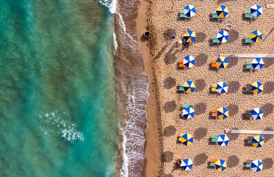 Concept of summer vacation. View from above, stunning aerial view of an amazing beach with beach umbrellas and turquoise clear water. Top view on a sun lounger under an umbrella on the sandy beach