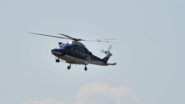 A police helicopter on a surveillance patrol against a clear blue sky, showcasing law enforcement in action.