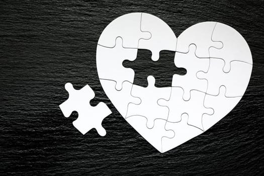 Heart-shaped jigsaw puzzle on color background. Puzzle heart on wooden background. A missing piece of the heart puzzle. Heart shape jigsaw puzzle. Puzzles in the shape of a heart. 