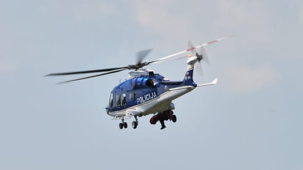 Dynamic image showcasing a blue police patrol helicopter in flight, with rotor blades in motion, set against a soft cloud background.