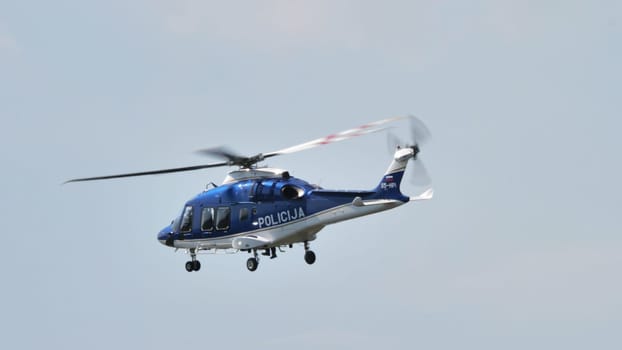A striking image of a police helicopter hovering with great detail of the undercarriage and markings against a blue sky backdrop.