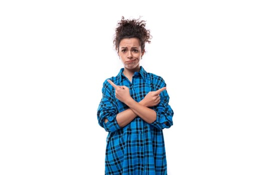 young upset curly brunette woman in a blue plaid shirt on a white background.