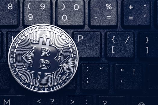 Bitcoin on compuer keyboard in background, symbol of electronic virtual money and mining cryptocurrency concept. Coin crypto currency bitcoin lies on the keyboard. Bitcoin on keyboard.