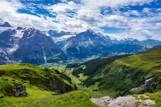 Grindelwald view and summer Swiss Alps mountains panorama landscape, green fields and high peaks in background, Switzerland, Bernese Oberland, Europe.