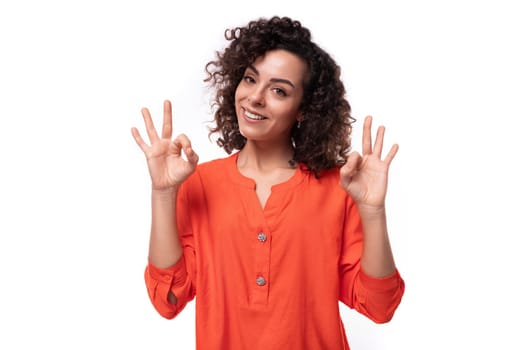 young successful european woman with curly black hair keeps dressed in a bright orange blouse.