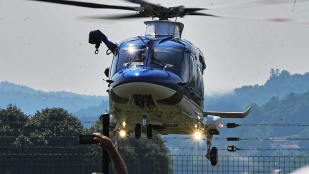 A blue Slovenian police helicopter performing a landing maneuver, captured from a dynamic angle with clear skies in the background. Copy space.