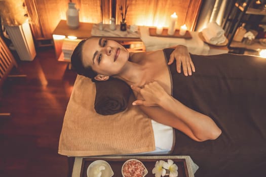 Caucasian woman customer enjoying relaxing anti-stress spa massage and pampering with beauty skin recreation leisure in warm candle lighting ambient salon spa at luxury resort or hotel. Quiescent