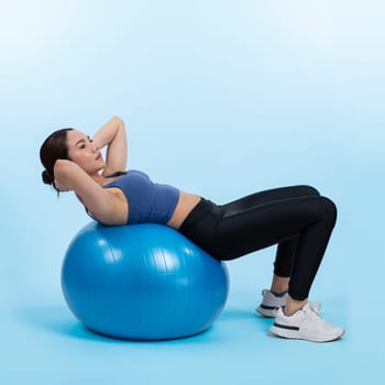 Young attractive asian woman portrait in sportswear with fit ball targeting on abs muscle for effective energetic daily workout routine. Studio shot and isolated background. Vigorous