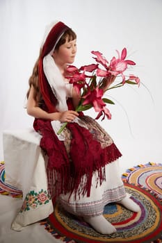 Portrait of Little girl in a stylized Tatar national costume with flowers on a white background in the studio. Photo shoot of funny young teenager who is not a professional model
