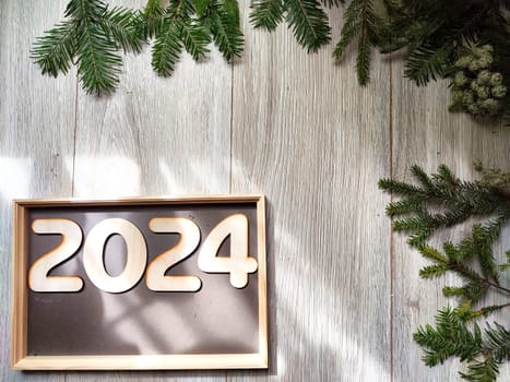 Wooden figures and numbers of the new year 2024 with frame and fir branches of Christmas tree. Celebration. Abstract background, pattern, frame, place for text, copy space