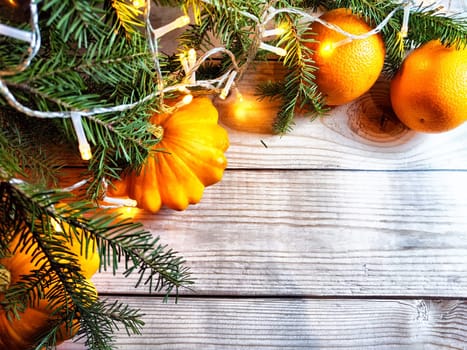 Festive decoration with bouquet and branches of spruce, bright glowing garlands, oranges on wooden background. Decor for Christmas and New Year. Abstract texture, frame, place for text and copy space