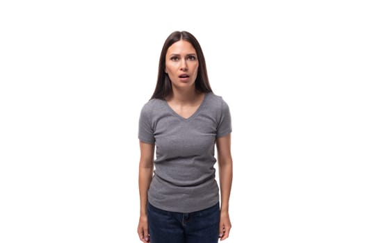 young surprised brunette promoter woman dressed in a gray t-shirt on a white background.