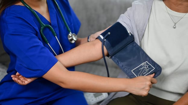 Healthcare worker measuring blood pressure middle age woman during home visit. Home health care service concept.