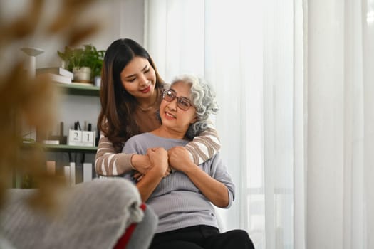 Affectionate young Asian woman hugging senior mother from back. International hug day concept.