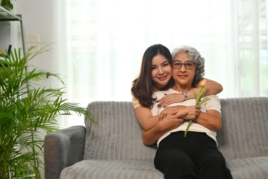 Affectionate young Asian woman hugging senior mother from back. International hug day concept.