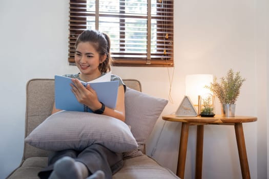 Happy young woman read book on sofa at home. Lifestyle freelance relax in living room. Lifestyle Concept.