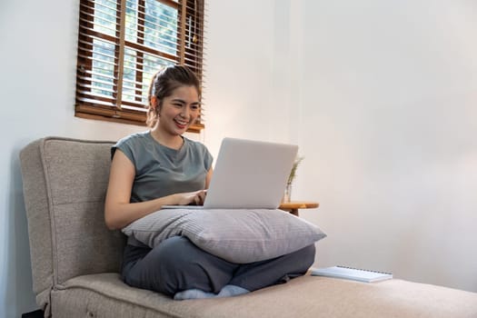 Young woman asian using laptop pc computer on couch relax surfing the net at home.