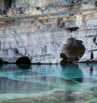 Stunning exterior view of a cave with a vertical cliff featuring layered textures above crystal clear blue waters.