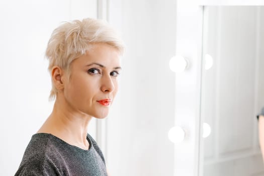 Beautiful woman with short haircut looking in mirror at her home