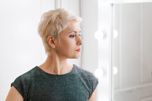 Beautiful woman with short haircut looking in mirror at her home