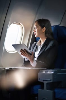 Successful Asian business woman, Business woman working in airplane cabin during flight on tablet.