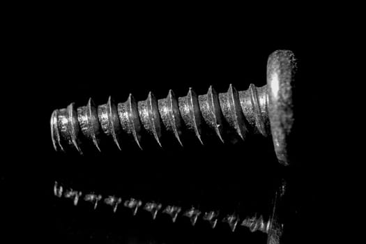 Macro image of a single coarse-threaded machine screw on a black background