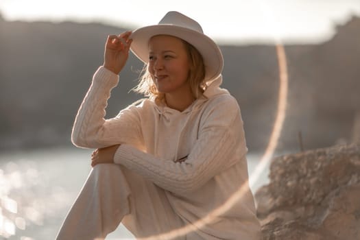 Happy blonde woman in a white suit and hat posing at the camera against the backdrop of the sea.