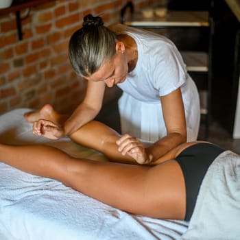 professional caucasian female physiotherapist masseuse performing leg massage to hispanic latino brunette woman in spa clinic