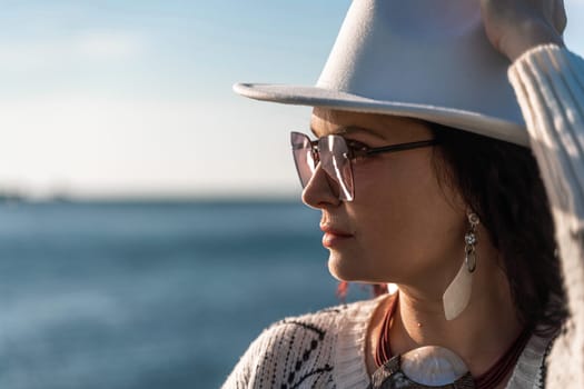 Portrait of a curly haired woman in a white hat and glasses on the background of the sea