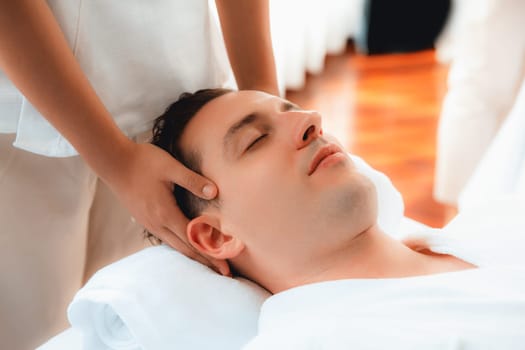 Caucasian man enjoying relaxing anti-stress head massage and pampering facial beauty skin recreation leisure in dayspa modern light ambient at luxury resort or hotel spa salon. Quiescent