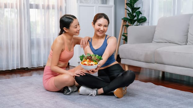 Young sporty Asian women in sportswear holding salad bowl together fill with vibrant of fruit and vegetable. Natural youthful and fit body lifestyle with balance nutrition and home exercise. Vigorous