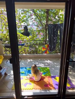 Little girl sits on a colorful rug on the terrace . High quality photo