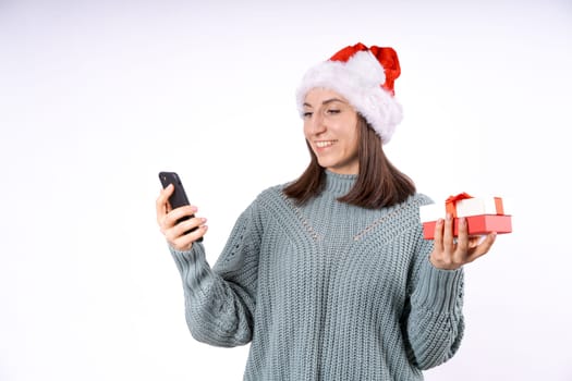 Portrait happy woman in santa hat and sweater holding gift box and phone on a white background