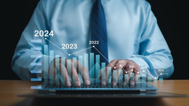 Stock trading. Finance. Investment. Growing business. A businessman in a suit puts his hands on a keyboard and shows a bar graph indicating business growth in 2024.