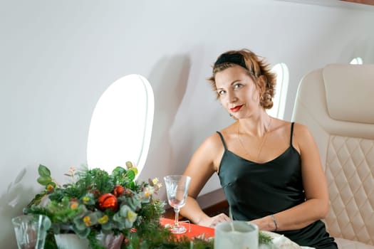 woman sits in private jet by illuminator, decorated for Christmas, New Year's Eve flight, holiday and travel concept.