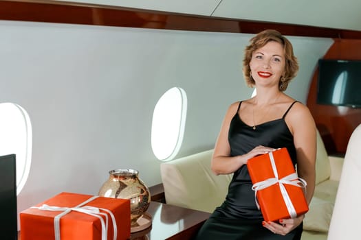 Woman sitting in private plane holding box with gift, for Christmas, New Year's Eve flight, holiday and travel concept