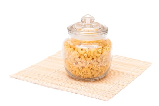 Uncooked Chifferi Rigati Pasta in Glass Jar on Bamboo Mat Isolated on White Background. Fat and Unhealthy Food. Scattered Classic Dry Macaroni. Italian Culture and Cuisine. Raw Pasta - Isolation