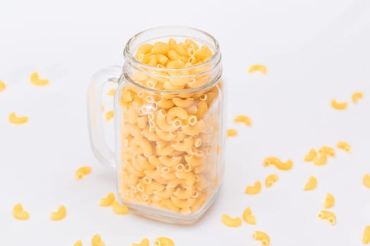 Uncooked Chifferi Rigati Pasta in Glass Jar on White Background. Fat and Unhealthy Food. Scattered Classic Dry Macaroni. Italian Culture and Cuisine. Raw Pasta