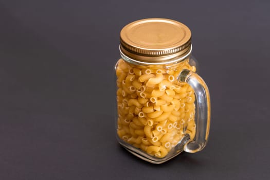 Uncooked Chifferi Rigati Pasta in Glass Jar on Black Background. Fat and Unhealthy Food. Classic Dry Macaroni. Italian Culture and Cuisine. Raw Pasta