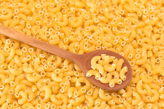 Uncooked Chifferi Rigati Pasta Background with Wooden Spoon. Fat and Unhealthy Food. Classic Dry Macaroni. Italian Culture and Cuisine. Raw Pasta