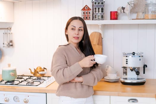 Concept festive Christmas atmosphere, cute woman drinking tea or coffee in a decorated kitchen wearing a sweater