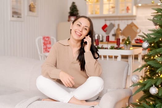Happy woman sits on couch holding cell phone, using cellular technology, shopping online, texting, relaxing on the couch in the cozy living room of her home.
