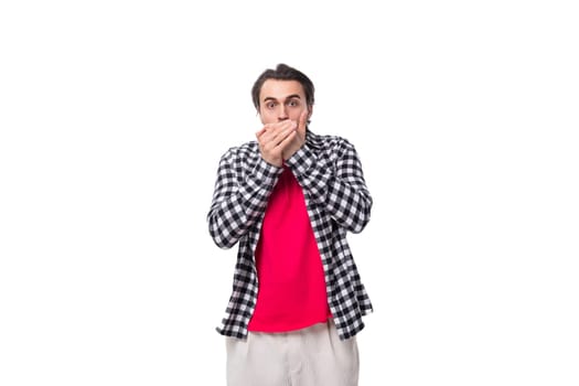 young surprised european brutal guy with chic hair and beard covered his mouth with his hand on a white background with copy space.
