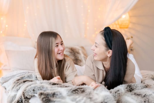 Happy mom and daughter cuddle on bed in decorated bedroom on Christmas Eve in anticipation of the party