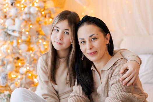 Happy mom and daughter cuddle on bed in decorated bedroom on Christmas Eve in anticipation of the party