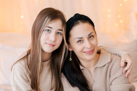 Happy mom and daughter cuddle on bed in decorated bedroom on Christmas Eve in anticipation of the party