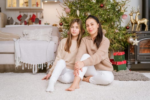 Mother and daughter sitting on the floor with a Christmas tree in the background